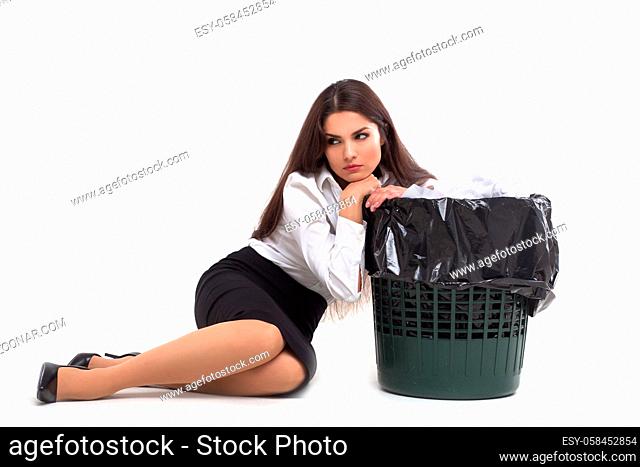 Attractive woman sitting down on floor next to garbage bin. Seductive lady wearing white blouse black skirt and black heels sitting down leaning on trash bucket...