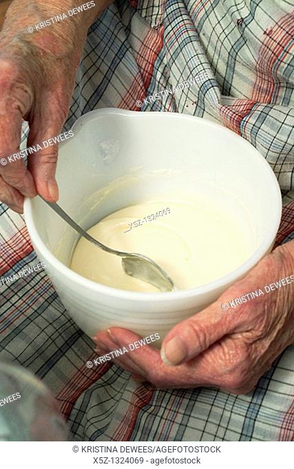 An old woman stirring homemade icing in a bowl on her lap