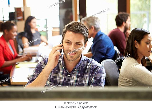 Male Architect Working At Desk With Meeting In Background