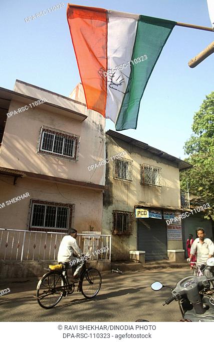People riding cycle and Indian tricolor election flag of congress political party street scene of Somvari bazaar ; Mulund Bombay Mumbai ; Maharashtra ; India