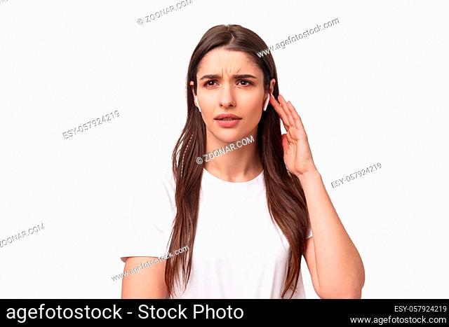 Close-up portrait of serious displeased young woman having troubles with using wireless earphone, have bad quality of sound, touching earbud to turn on song