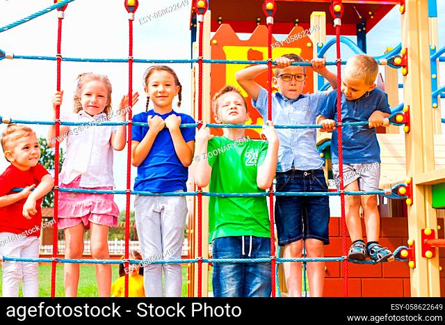 Six happy kids standing and holding the ropes of climbing net. Rope based playground in children amusement park