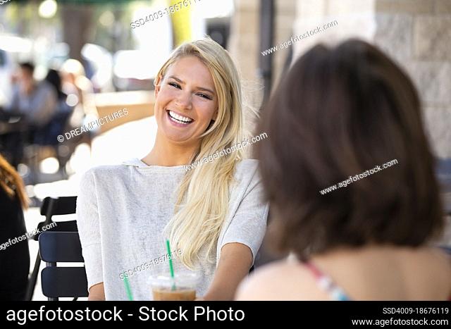 Two friends sitting outside a cafe laughing