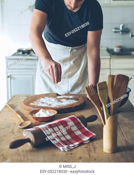 Chef making food on kitchen table. Baker man baking homemade bread dough on vintage wooden board. Retro style image. People cooking in home concept