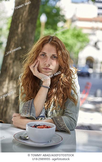 Young redhead woman sitting out with hands in cheek