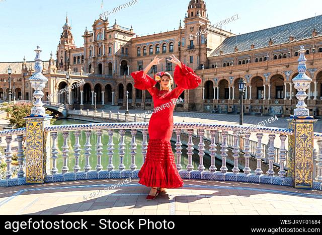 Female flamenco artist dancing with hands raised at Plaza De Espana in Seville, Spain on sunny day