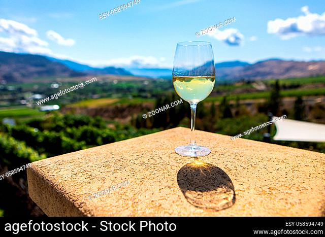 A Canadian glass of white wine on building top selective focus view against vineyard background, Okanagan Valley, British Columbia, Canada