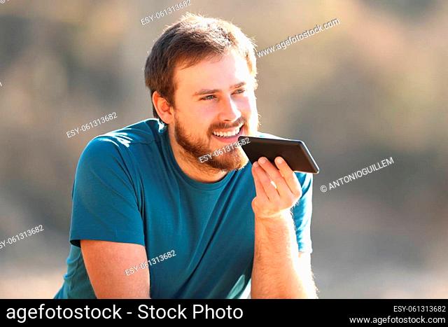 Happy man using voice recognition on cellphone contemplating outdoors