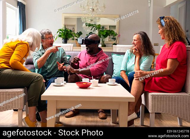 Happy multiracial senior man and women looking at male friend using vr headset at home