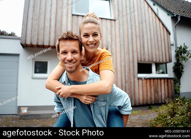 Happy man giving piggyback ride to blond girlfriend at backyard