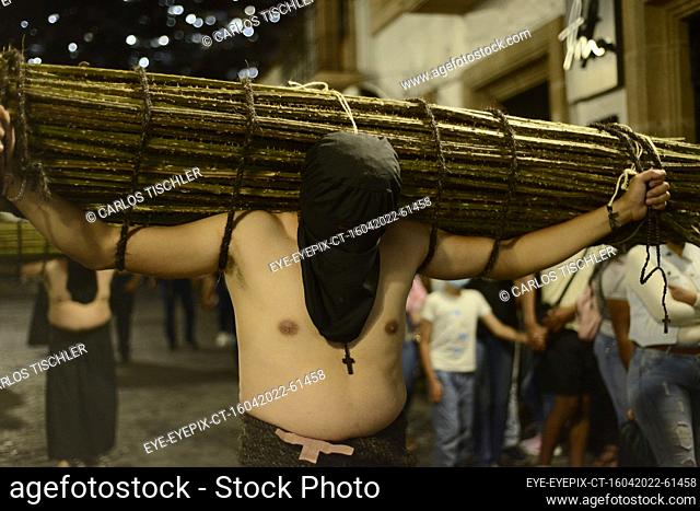 TAXCO, MEXICO - APR 15, 2022: A penitent wears a black hood, while lifts a roll of blackberry thorns weighing more than 50 kg