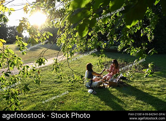 14 August 2021, Brandenburg, Neuhardenberg: Two young women sit with a picnic basket on a meadow in Neuhardenberg Castle Park