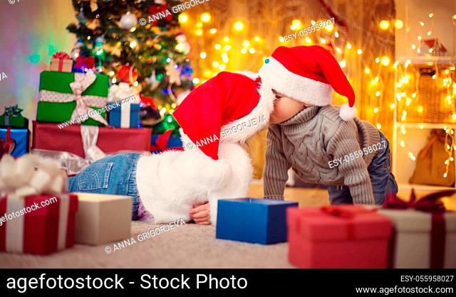 Boy and girl lying on the floor with presents near christmas tree. Children in red hats at home in winter