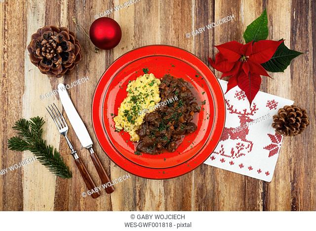 Plate of cooked venison goulash with mashed potatoes and Christmas decoration on wooden background