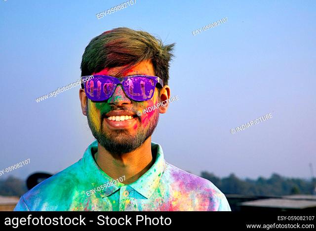 A SMILING YOUNG MAN WITH GOGGLES HAPPILY POSING DURING HOLI CELEBRATIONS