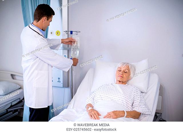 Doctor adjusting iv drip while patient lying on bed