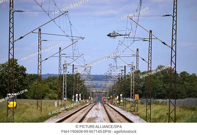 08 June 2019, Bavaria, Meitingen: A helicopter transports a railway signal pole over the railway line Augsburg-Donauwörth