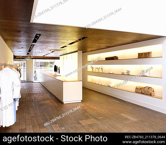 Interior of retail designer clothes shop metal clothes rail neatly lined with men? clothes Interiors shops retailing long white wooden bench with wooden top...