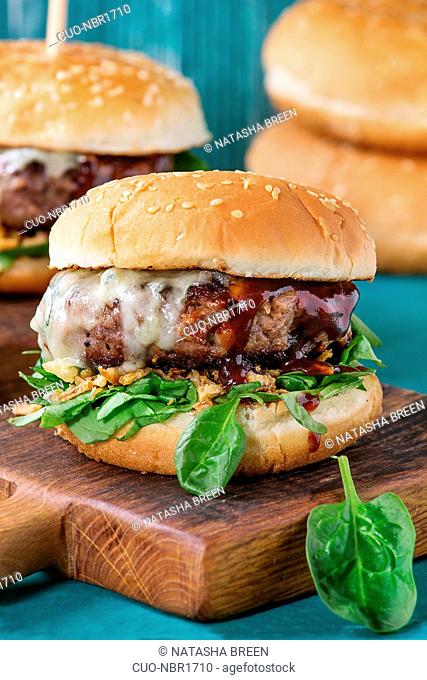Two hamburgers with beef burger cutlet, fried onion, spinach, ketchup sauce and blue cheese in traditional buns, served on wood chopping board over bright...
