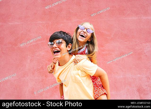 Cheerful boy piggybacking female in front of red wall