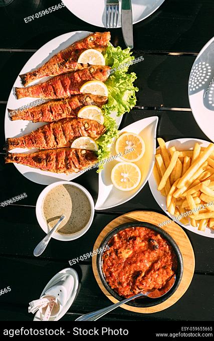 Batumi, Adjara, Georgia. Dishes Of Georgian National Cuisine: Fried Red Mullet Fish, Lemons, Satsivi Or Walnut Sauce, Stewed Mussels And French Fries
