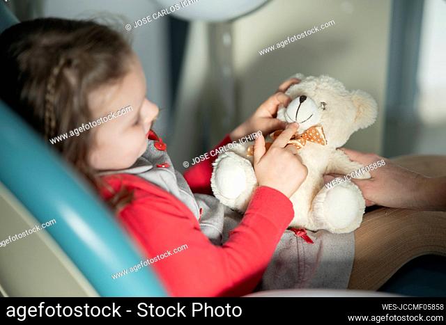Little girl sitting on dental chair with stuffed toy at medical clinic