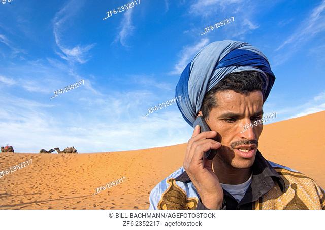 Morocco Sahara Desert sand dunes portrait of local man with turbin on cell phone in Las Palmeras area