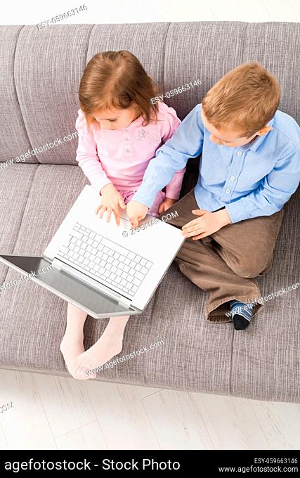 Overhead shot of children sitting on couch at home, browsing internet on laptop computer, looking at screen