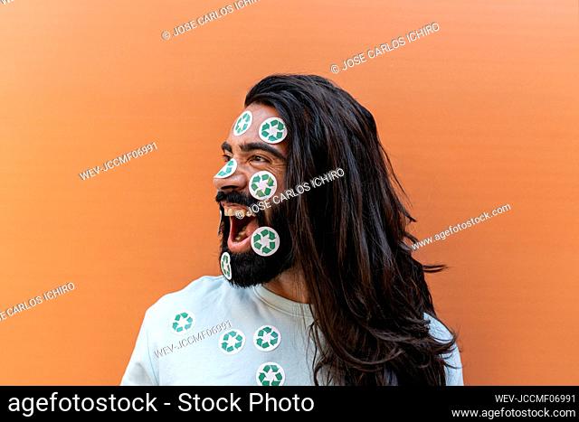 Shouting bearded man with recycling stickers on face in front of wall
