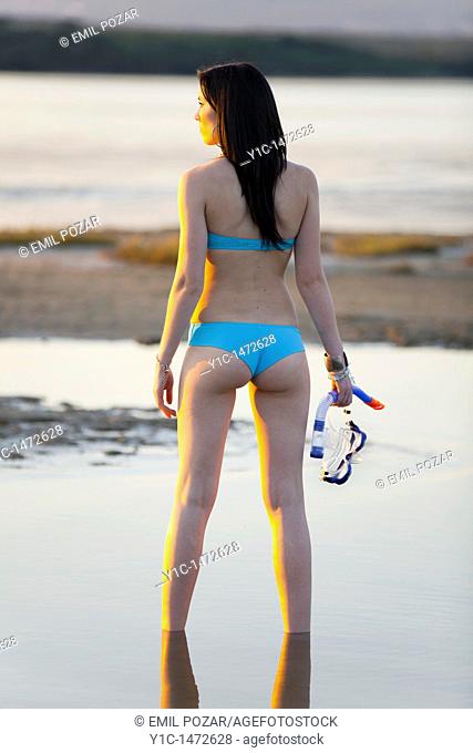 Attractive young woman on the beach with a diving mask in hand, watching sunset