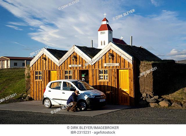 Man kneeling next to a car checking the tyre pressure, petrol station in a wooden hut, Moeðrudalur, Highlands of Iceland, Iceland, Europe