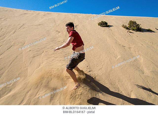Caucasian teenage boy sliding on sand dune
