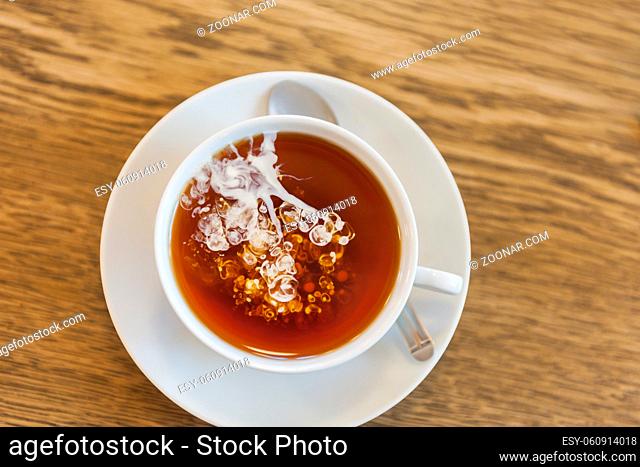 Top View Closeup of a white cup of tea with freshly poured cream spreading in a cloudy shape. This form of tea preparation became a tradition in northern...