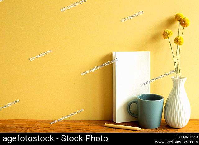 Notebook, mug cup, pencil, vase of dry flowers on wooden desk. yellow wall background. workspace