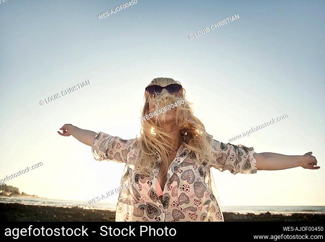 Carefree young woman covering face with hair while dancing at beach against clear sky