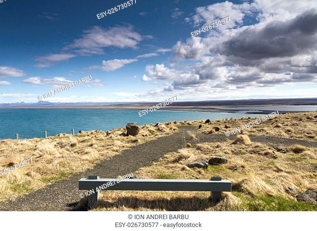 Horizontal panorama of a wooden resting bench with a beautiful shoreline in the background and dramatic clouds above