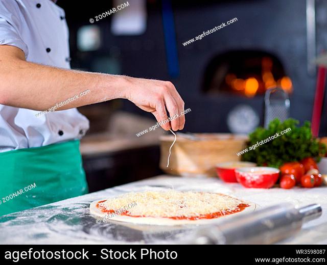 chef sprinkling cheese over fresh pizza dough on kitchen table