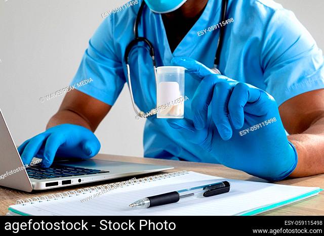 African american male health worker wearing face mask holding medication container using laptop