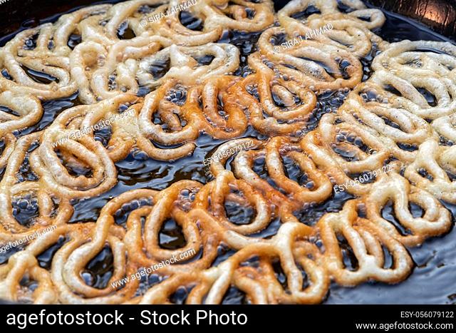 Frying Jalebi batter in oil. Red and orange-colored batter will be dipped into sugar syrup for a sweet taste. Jalebi is a popular sweet snack