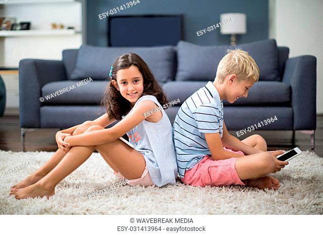 Siblings sitting back to back while boy using digital tablet