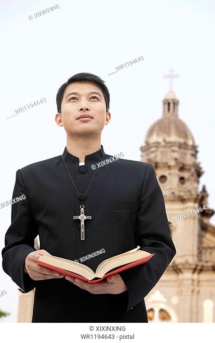 Young Priest Looking to Sky in Front Of Church