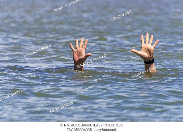 pair of masculine hands sticks out of the sea water on a summer day, a gesture of a man who sinks