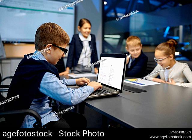 Meeting of smiling diverse kid business team. Focus on little computer genius typing keyboard laptop