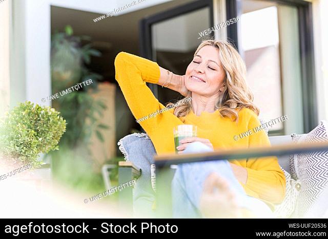 Portrait of smiling mature woman relaxing on terrace with green smoothie