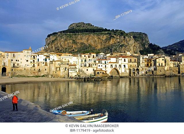 Old port Mt. La Rocca, fishing boats vessels, man in red coat, moorish architecture town of Cefalu, Province of Palermo, Sicily, Italy