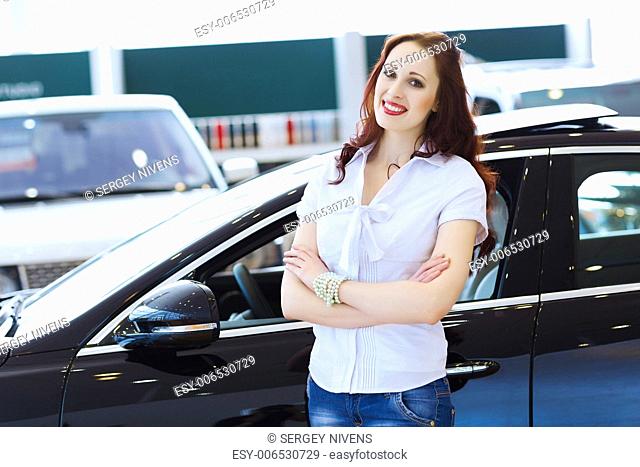 Pretty woman standing near car at car center. Choosing a car
