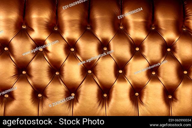Background texture of dark golden brown capitone genuine leather, retro Chesterfield style soft tufted furniture upholstery with deep diamond pattern and...
