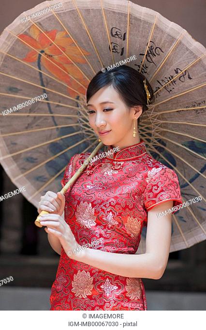 Young woman with cheongsam holding paper parasol and looking down