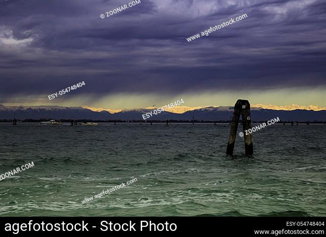 View of Venice Lagoon with dramatic overcast stormy sky and horizon in the distance sunlit peaks of Dolomite Alps, Venice, Italy