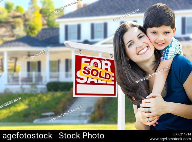 Young mother and son in front of sold for sale real estate sign and house